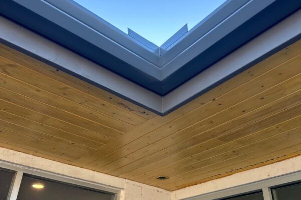 Close-up of a modern home exterior showcasing a wooden ceiling and sleek metal roof edges against a clear blue sky.