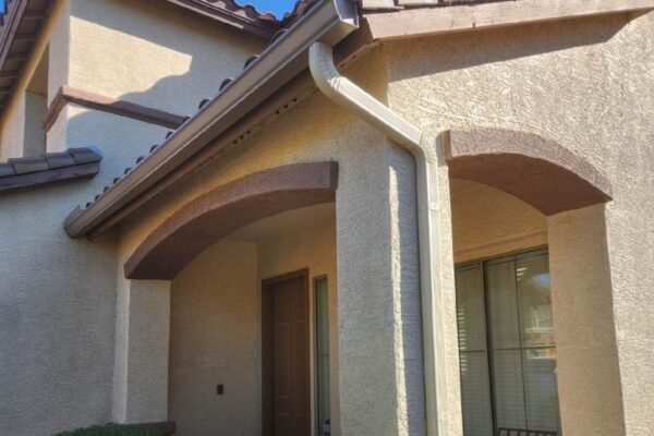 Close-up of a home's exterior featuring arches, a brown roof, and a light-colored wall with landscaping.