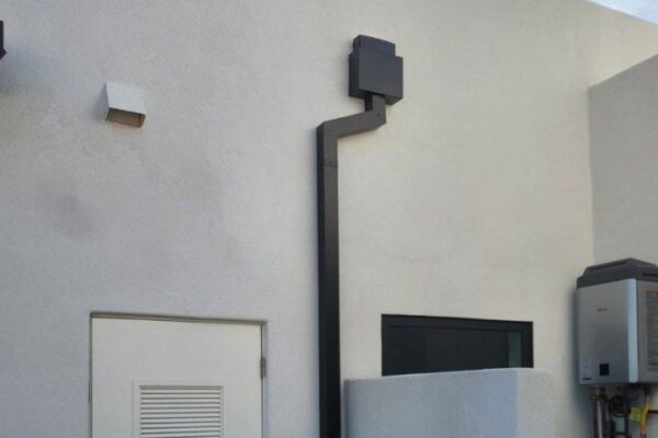 Black conduit and wall-mounted equipment against a light-colored exterior, showcasing modern building utility features.
