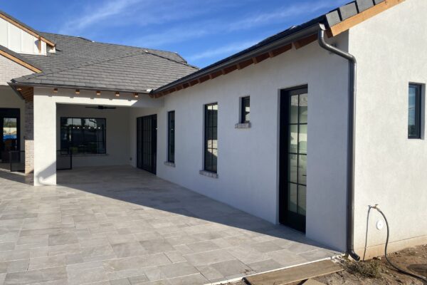 Modern home exterior showcasing a spacious patio with stone tiles and large windows under a blue sky. Perfect for outdoor living.