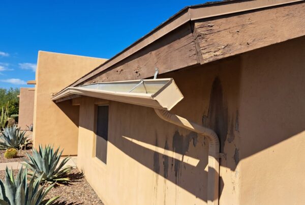 Close-up of a home's exterior showing wear on fascia and gutter, with desert landscaping and clear blue sky.