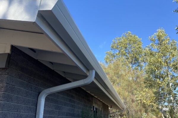 Gutter systems on a home’s roof with clear blue sky and surrounding greenery. Ideal for discussing drainage solutions.