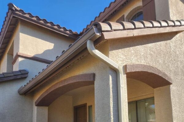Modern home exterior featuring a tiled roof, decorative arches, and a downspout against a clear blue sky.