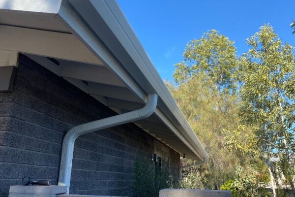 Gutter system on residential building, featuring downspouts and surrounding greenery under a clear blue sky.